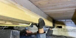 Afbeelding van een man die aan het werk is in een kruipruimte, gericht op het herstellen van balken.