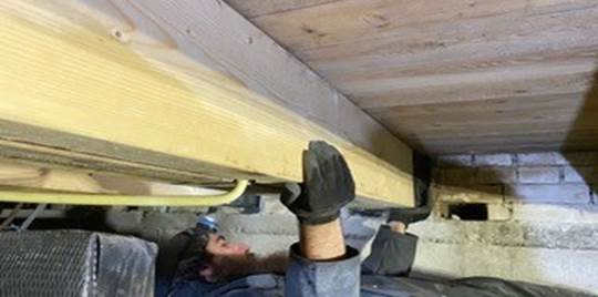 Afbeelding van een man die aan het werk is in een kruipruimte, gericht op het herstellen van balken.